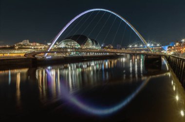 Newcastle, İngiltere - 13 Nisan 2025 - Arkaplanda Tyne Köprüsü ile Tyne Nehri 'ni kaplayan Iconic Gatehead' in Gece Görüşü. Nehirde yansıması olan yaya köprüsünü duvar kağıdı, poster ve S olarak kullanın.