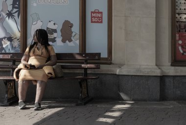 Windsor, İngiltere - 2003 Nisan 2025 - Miniso mağazasının önündeki ahşap bir bankta oturan ve elinde telefon tutan siyah elbiseli Afro-Amerikan kadınları. Metin, Seçici odak için Duvar Kağıdı, Poster ve Boşluk olarak kullan.