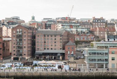 Newcastle, İngiltere - 11 Nisan 2025 - Quayside bölgesindeki eski binalar ve Newcastle 'daki Sage Gateshead' den (The Glasshouse International Centre for Music) Tyne 'daki Tyne manzaralı insanlar. Metin için duvar kağıdı, poster ve boşluk olarak kullan.