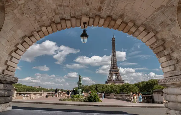 Fransa, Paris - 3 Mayıs 2025 - Paris 'teki Eyfel kulesinin arka planda mavi gökyüzü ve bulutlu manzarası, Pont de Bir Hakeim' in merkezinde tuğla yapılar bulunan bir köprünün kemerinden görülüyor. Duvar kağıdı, poster ve boşluk olarak kullan