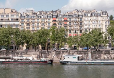 Fransa, Paris - 3 Mayıs 2025 - Arkasında Haussmannian mimari konut binaları olan nehir kıyıları boyunca kıyıya yanaşan nehir kruvazörü manzarası. Metin, Seçici odak için Duvar Kağıdı, Poster ve Boşluk olarak kullan.
