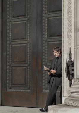 Londra, İngiltere - 13 Mayıs 2025 - Takım elbiseli bir adam kapı eşiğine dayanmış, Haruki Murakami kitabı okuyor. Metin, Seçici odak için Duvar Kağıdı, Poster ve Boşluk olarak kullan.