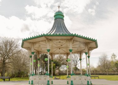 Newcastle, İngiltere - 13 Nisan 2025 - Bir Orkestra Sahnesi ve Bir Tribün Görünümü. Leazes parkına monte edilmiş Viktorya dönemi orkestrasının modern bir kopyası. Arka planda yeşil ağaçlar olan Müzik Pavyonu, bunu duvar kağıdınız olarak kullanın..