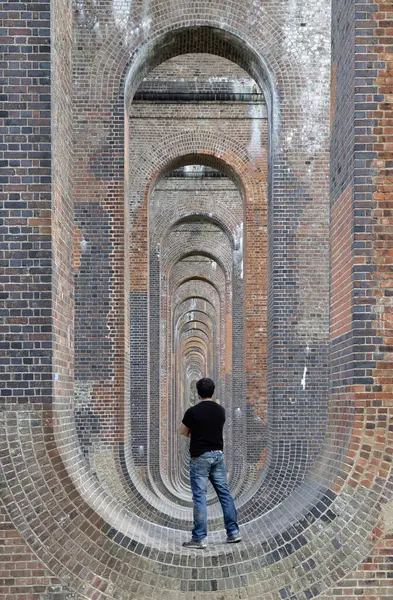 Sussex, İngiltere - 21 Mayıs 2025 - Ouse Viyadük veya Balcombe Viaduct köprüsünün altındaki yapıda siyah tişört ve kot giyen bir gencin arka planı 