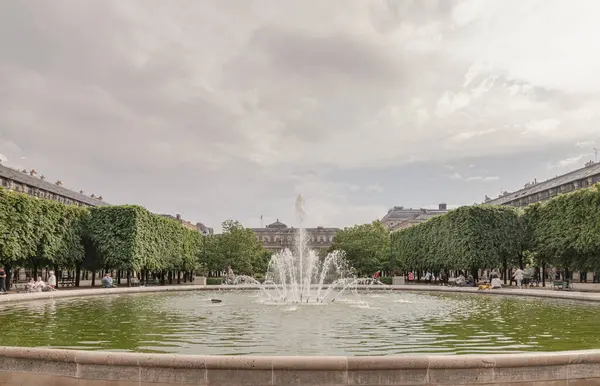 Fransa, Paris - Mayıs 03, 2025 - Arka planda Palais Royal binası ve gökyüzü olan Jardin du Palais Royal çeşmesinin manzarası. 