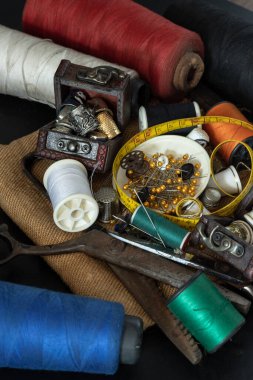 Çeşitli renklerde iplikler, küçük ahşap hazine sandığında yüksükler, çelik makas, yeşil minyatür makaralara sıkışmış iğneler, iplik ve mezura şeritleri, çuval bezinde küçük yuvarlak tepsilerde bulunan raptiyeler. Ögeler ayarlanıyor veya nesne dikiliyor