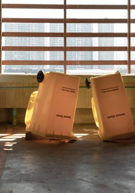 Büyük plastik çöp konteynırını temizledikten sonra kuruyana kadar baş aşağı çevirme görüntüsü. Dairenin otoparkındaki beton duvarın yanındaki büyük, sarı plastik çöp kutusu, genel atık için kapağı olan plastik çöp, duvar kağıdı olarak kullanın..