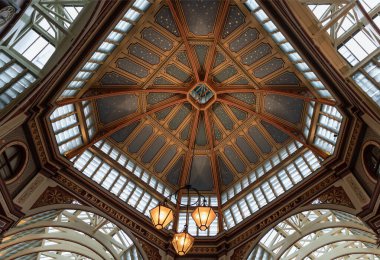 Londra, İngiltere - 27 Haziran 2025 - Tavanın dekoratif Viktorya dönemi mimarisi ve Leadenhall Pazarı içindeki renkli dekorasyonlar. Süslü, işlenmiş demir, cam çatının doğal ışığın pazar alanını aydınlatmasına olanak sağlayan bir kombinasyonu. Metin için boşluk.