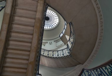 Londra 'daki Somerset Evi' ndeki Nelson Merdiveni 'ne baktığımızda, neoklasik bir binanın içindeki sarmal bir merdiven, üst kısmında belirgin dairesel bir oktulus (tavan penceresi) ve parmaklıklarda karmaşık, süslü bir demiri barındırıyor. Boşluğu kopyala.