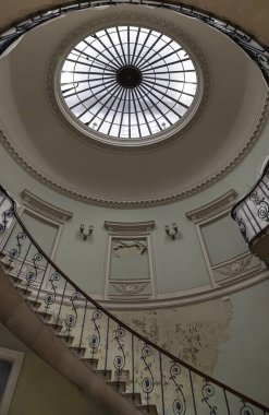 Londra 'daki Somerset Evi' ndeki Nelson Merdiveni, neoklasik bir binanın içindeki büyük sarmal bir merdiven, üst kısmında belirgin dairesel bir oktulus (tavan penceresi) ve parmaklıklarda karmaşık, süslü demirlerden oluşan bir merdiven. Metin için boşluk.