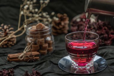 Roselle çayı (Jamaika doru, Rozelle veya hibiscus sabdariffa) bir çaydanlıktan kuru roselle ve kahverengi baston şeker küpüyle cam bardağa dökülür. C vitamini ve minerallerle dolu sağlıklı bitki çayı. Sağlık kavramı. Organik ve Yaz içeceği, Drin.