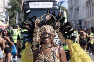 Sanatçı, Notting Hill Karnavalı 'nın büyük, tüylü başlığı ve süslü mücevherleriyle süslü renkli ve çetrefilli bir kostüm giyerek Karayip kültürü ve tarihi kutlamalarıyla tanınıyor.