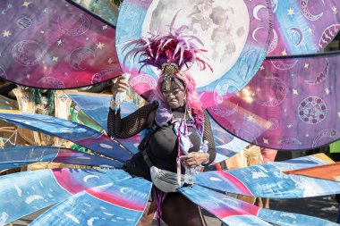 Sanatçı, Notting Hill Karnavalı 'nın büyük, tüylü başlığı ve süslü mücevherleriyle süslü renkli ve çetrefilli bir kostüm giyerek Karayip kültürü ve tarihi kutlamalarıyla tanınıyor.