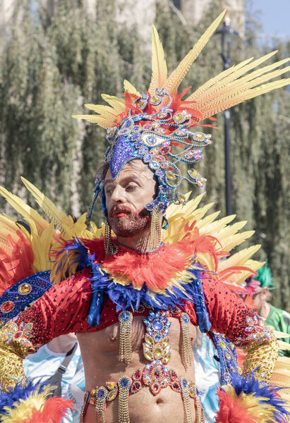a performer at the Notting Hill Carnival in West London, adorned in a vibrant and intricate costume featuring a large, feathered headdress and ornate jewelry. The Notting Hill Carnival is widely recognized for its celebration of Caribbean culture.