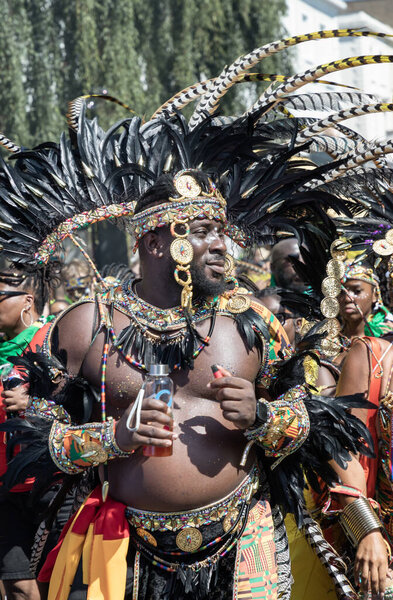 a performer at the Notting Hill Carnival in West London, adorned in a vibrant and intricate costume featuring a large, feathered headdress and ornate jewelry. The Notting Hill Carnival is widely recognized for its celebration of Caribbean culture.