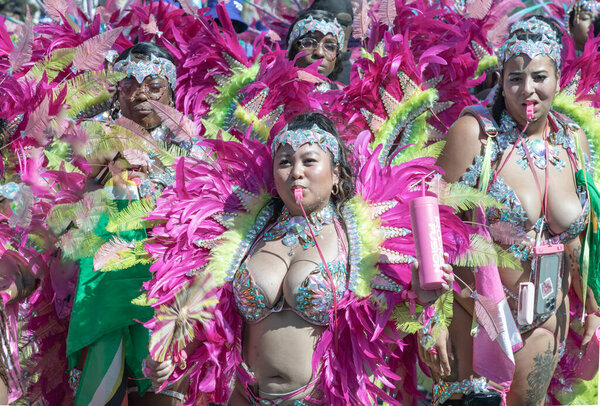 The performer is adorned in colorful and intricate costume featuring large, feathered headdress and ornate jewelry in the Notting Hill Carnival is renowned for its celebration of Caribbean culture and history, featuring parades with elaborate costume