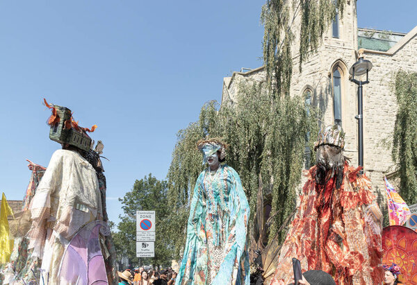 Performance three individuals in elaborate, distinct costumes and a detailed headpiece resembling a headdress with horns or spikes at the Notting Hill Carnival in West London, its widely recognized for its celebration of Caribbean culture and history