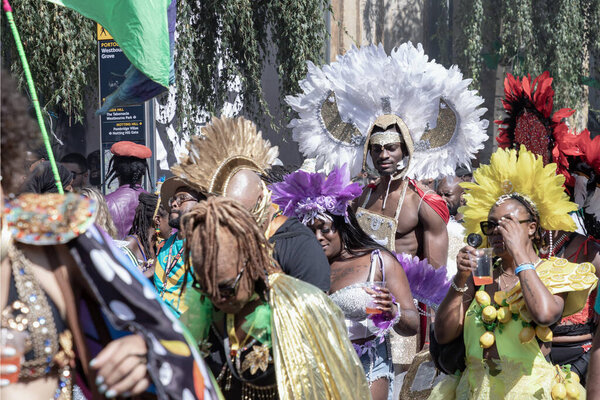 a performer at the Notting Hill Carnival in West London, adorned in a vibrant and intricate costume featuring a large, feathered headdress and ornate jewelry. The Notting Hill Carnival is widely recognized for its celebration of Caribbean culture.