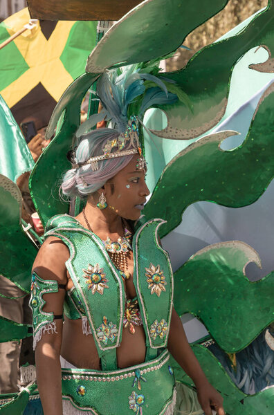 a performer at the Notting Hill Carnival in West London, adorned in a vibrant and intricate costume featuring a large, feathered headdress and ornate jewelry. The Notting Hill Carnival is widely recognized for its celebration of Caribbean culture.
