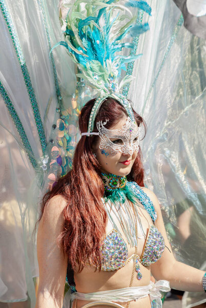 a performer at the Notting Hill Carnival in West London, adorned in a vibrant and intricate costume featuring a large, feathered headdress and ornate jewelry. The Notting Hill Carnival is widely recognized for its celebration of Caribbean culture.