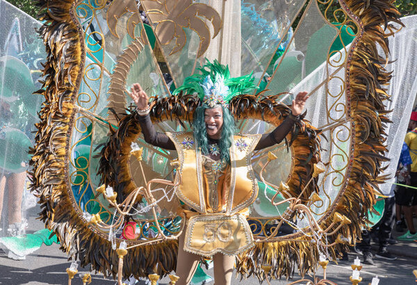 a performer at the Notting Hill Carnival in West London, adorned in a vibrant and intricate costume featuring a large, feathered headdress and ornate jewelry. The Notting Hill Carnival is widely recognized for its celebration of Caribbean culture.
