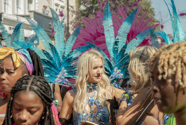 a performer at the Notting Hill Carnival in West London, adorned in a vibrant and intricate costume featuring a large, feathered headdress and ornate jewelry. The Notting Hill Carnival is widely recognized for its celebration of Caribbean culture.