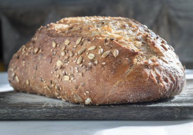 Organik Sourdough somunu, organik malzemelerin kullanımı ve kabak, ayçiçeği, susam ve keten tohumu gibi çeşitli tohumların ahşap bir kesim tahtasının üzerinde dinlenmesi ile karakterize edilir. Metin için duvar kağıdı, poster ve boşluk olarak kullan.