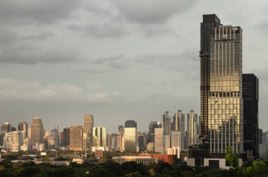 Bangkok 'ta günbatımında bulutlu bir gökyüzüne karşı modern gökdelenler. Ön plandaki en önemli bina IDEO Morph 38 veya Ashton Kulesi olarak tanımlanmıştır. Arkaplan daha geniş bir şehir manzarası ortaya çıkarıyor.
