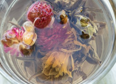 Çiçek açan çayın (çiçek açan çay veya sanatsal çay) yakın çekimi. Kurutulmuş çay yapraklarından yapılan el yapımı çay türüdür. Kurutulmuş, yenilebilir çiçeklerin etrafına sarılmış. Aranth, kasımpatı ya da gül gibi. Sıcak suda demlendiğinde, çay topu yavaşça açılır.