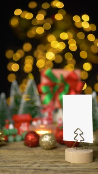 以白色贺卡或邀请卡为礼物的圆形圣诞礼品盒 其背景为木制桌子上的圣诞前夜派对 配有圣诞装饰品和Bokeh灯 — 图库视频影像
