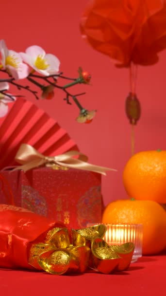 中国の旧正月の背景のループ シルクバッグの金 金の弓 紙のファン オレンジ 梅の花の枝 ろうそくおよび赤い浮遊ランタンの揺れが付いている赤いギフト用の箱 バーティカル — ストック動画