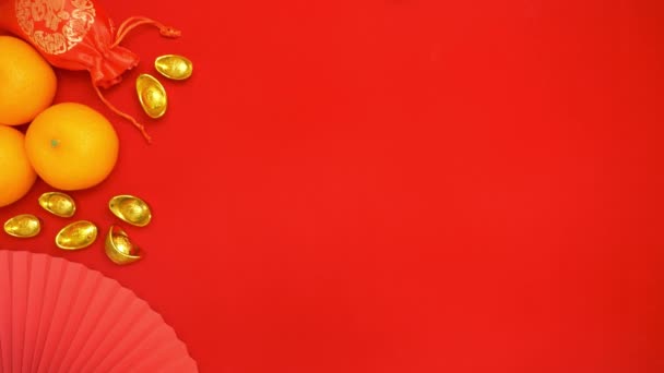 中国の旧正月のお祝いの赤い背景にラッキーアイテムの装飾の装飾とお金を与えるためにトップから手を保持するフラットレイループ映像 — ストック動画