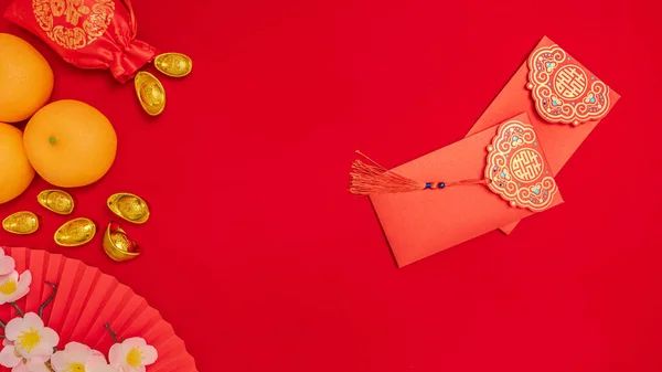 Chinese Lunar New Year background, red theme. silk bag with ancient gold bar, orange, paper hand fan, plum blossom branch, red envelope, Tae Eia, ang pow for giving money on Chinese new year celebrate