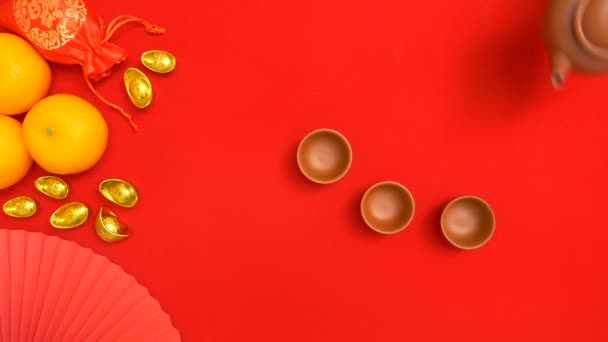 中国农历新年庆祝活动期间 手持茶壶向茶杯中倒入橙子 中国古代金条 丝袋装饰装饰品 平铺红色底色 — 图库视频影像