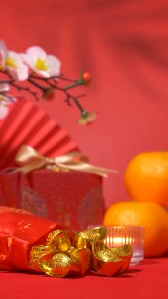 中国の旧正月の背景のループ シルクバッグの古代中国の金の棒 金の弓 紙のファン オレンジ 梅の花の枝 ろうそくおよび葉の影の揺れが付いている赤いギフト用の箱 バーティカル — ストック動画