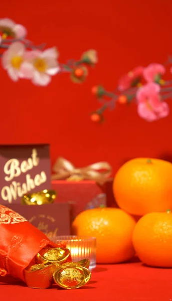 Chinese Lunar New Year red background. ancient Chinese ingot gold bar in silk bag, gift box with text best wishes, orange, paper fan, plum blossom, candle sway on Chinese new year celebrate