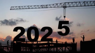 5 numaralı vinç kaldırma 2025 'e iniyor, 2025 yılının başlangıcına hazırlanın siluet inşaat sahası ve işçi ekibi birlikte çalışacak, arka planda gün doğumu gökyüzü