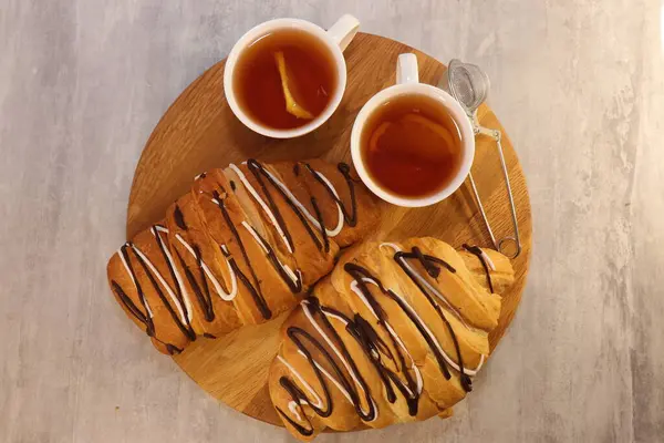 İki bardak limonlu çayın yanında çikolata serpiştirilmiş taze aromatik kruvasan. Çikolatalı fırın ürünü ve sağlıklı çay.