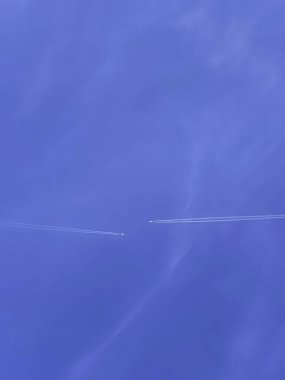 Açık mavi gökyüzünde, arka planda soluk bulutlarla süzülen bir uçağın minimalist görüntüsü.