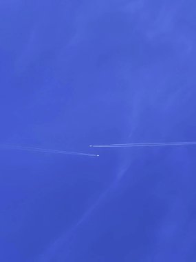 Açık mavi gökyüzünde, arka planda soluk bulutlarla süzülen bir uçağın minimalist görüntüsü.