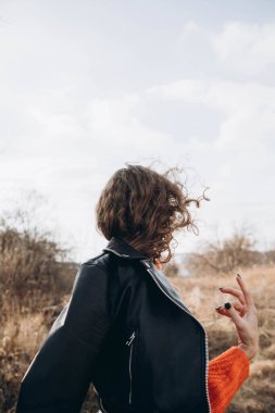 Sonbahar parkının arka planında güzel gülüşler kıvırcık esmer. Sonbahar doğasının arka planına karşı turuncu kazaklı genç kıvırcık kız.