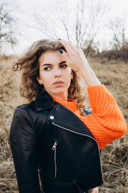 Sonbahar parkının arka planında güzel gülüşler kıvırcık esmer. Sonbahar doğasının arka planına karşı turuncu kazaklı genç kıvırcık kız.