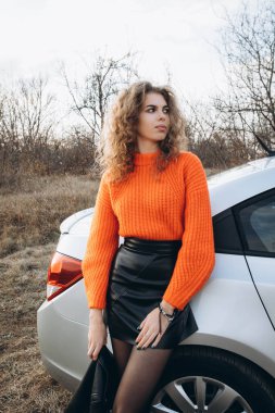 Sonbahar parkının arka planında güzel gülüşler kıvırcık esmer. Sonbahar doğasının arka planına karşı turuncu kazaklı genç kıvırcık kız.