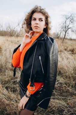 Sonbahar parkının arka planında güzel gülüşler kıvırcık esmer. Sonbahar doğasının arka planına karşı turuncu kazaklı genç kıvırcık kız.