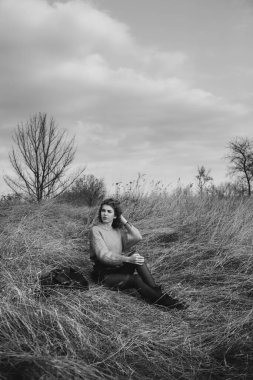 Sonbahar parkının arka planında güzel gülüşler kıvırcık esmer. Sonbahar doğasının arka planına karşı turuncu kazaklı genç kıvırcık kız.