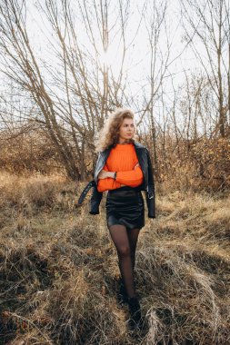 Sonbahar parkının arka planında güzel gülüşler kıvırcık esmer. Sonbahar doğasının arka planına karşı turuncu kazaklı genç kıvırcık kız.