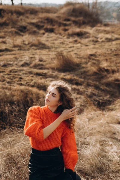 stock image Against the background of autumn park smiles beautiful smile curly brunette. young curly girl in an orange sweater against the backdrop of autumn nature