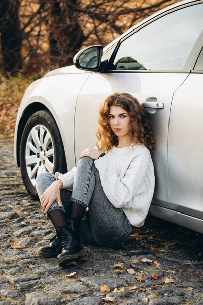 stock image young curly girl in a white sweater against the backdrop of autumn nature and her own car. High quality photo