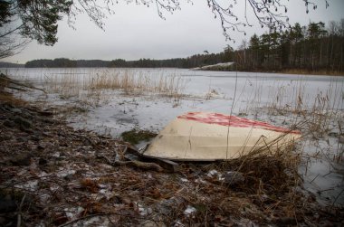 Bir kış günü donmuş bir gölün kıyısında alabora olmuş bir tekne.