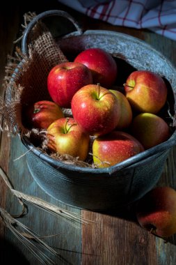 Tahta bir masada eski bir kasede kırmızı elmalar.
